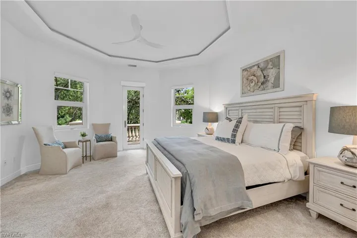 Bedroom with multiple windows, access to outside, a tray ceiling, and light colored carpet