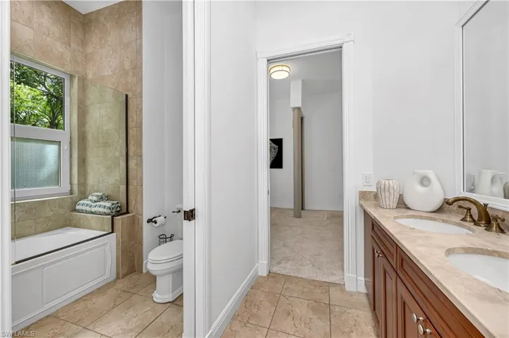 Bathroom with a bath, toilet, a sink, double vanity, and baseboards