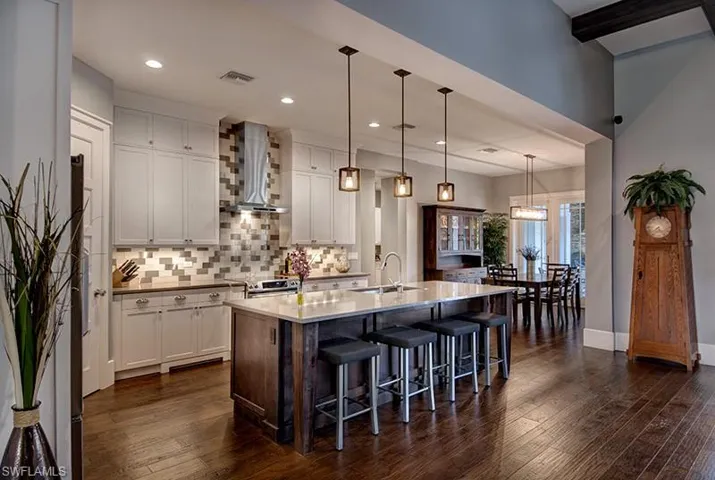 Kitchen with sink, a center island with sink, white cabinetry, and wall chimney range hood