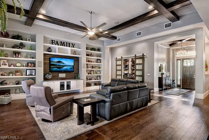 Living room with built in features, a barn door, beam ceiling, and dark hardwood / wood-style flooring