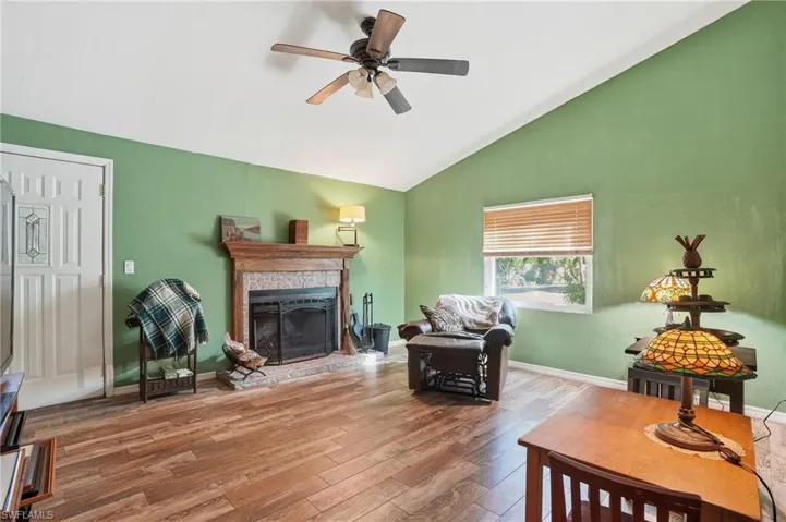 Living area with vaulted ceiling, hardwood / wood-style flooring, a fireplace with raised hearth, and a ceiling fan