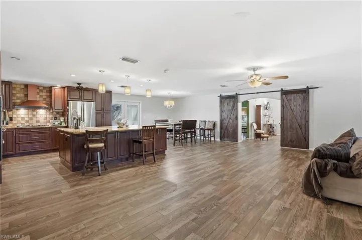 Kitchen featuring a barn door, open floor plan, an island with sink, a kitchen bar, and pendant lighting