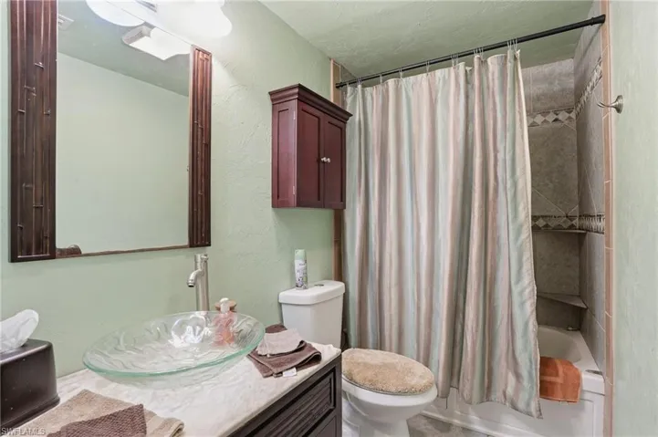 Bathroom with a textured wall, shower / tub combo, vanity, and a textured ceiling