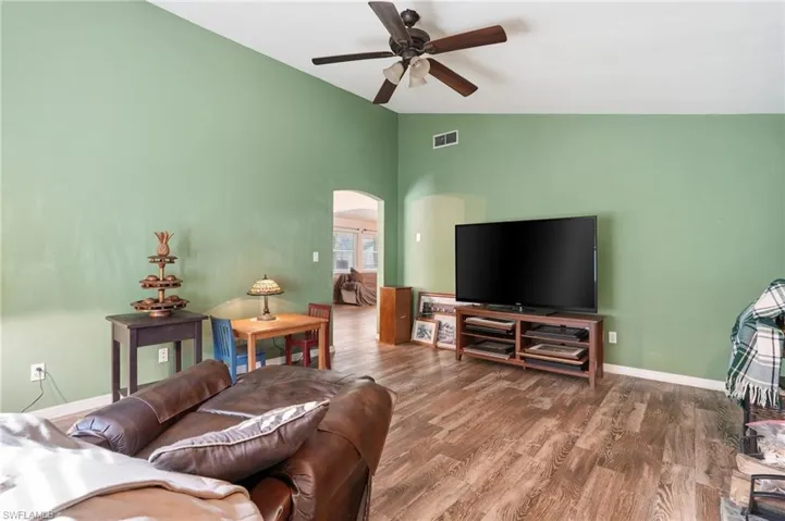 Living area featuring arched walkways, vaulted ceiling, wood finished floors, and ceiling fan