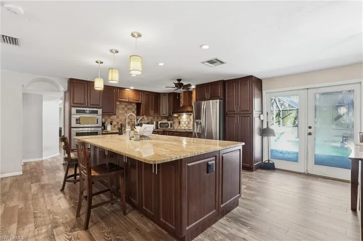 Kitchen featuring dark wood finish cabinets, decorative light fixtures, light stone counters, a spacious island, and stainless steel appliances