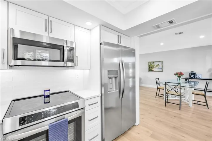 Kitchen with stainless steel appliances, white cabinetry, light wood-style floors, backsplash, and recessed lighting