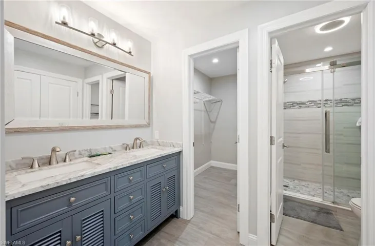 Full bathroom with a stall shower, double vanity, a walk in closet, and light wood finished floors