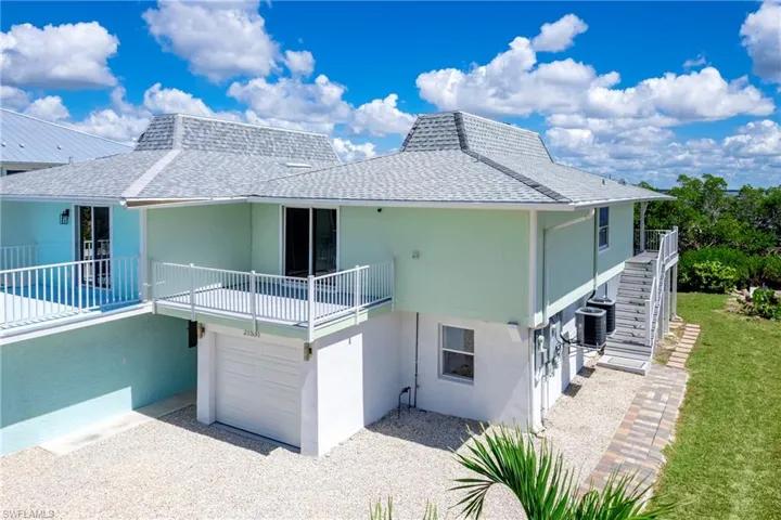 Back of property featuring roof with shingles, stairs, stucco siding, and gravel driveway