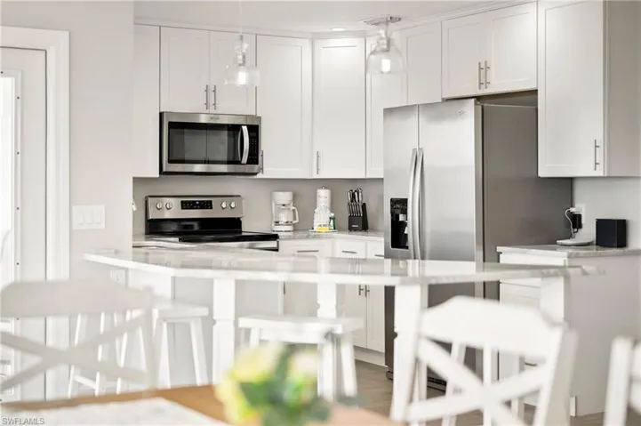 Kitchen with a kitchen bar, appliances with stainless steel finishes, white cabinets, pendant lighting, and light stone counters
