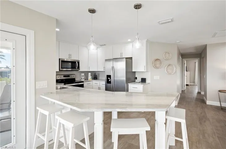 Kitchen with a peninsula, stainless steel appliances, white cabinetry, light stone countertops, and recessed lighting