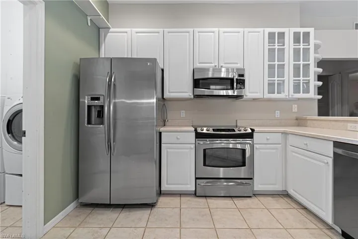 Kitchen with light tile patterned flooring, white cabinetry, washer / clothes dryer, and appliances with stainless steel finishes