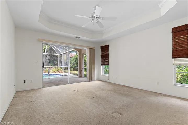 Empty room with ceiling fan, a tray ceiling, ornamental molding, and light colored carpet