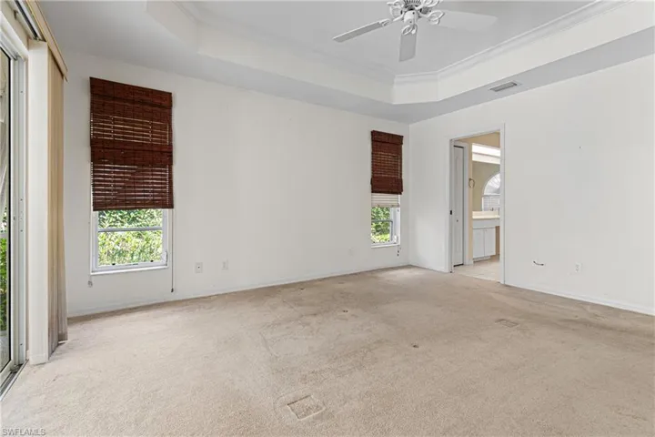 Primary bedroom featuring ceiling fan, light colored carpet, ornamental molding, and a tray ceiling