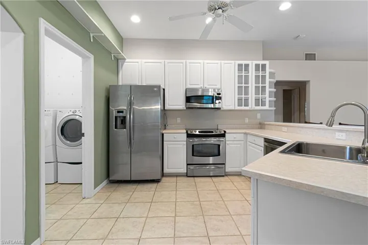 Kitchen with stainless steel appliances, sink, light tile patterned floors, white cabinetry, and ceiling fan