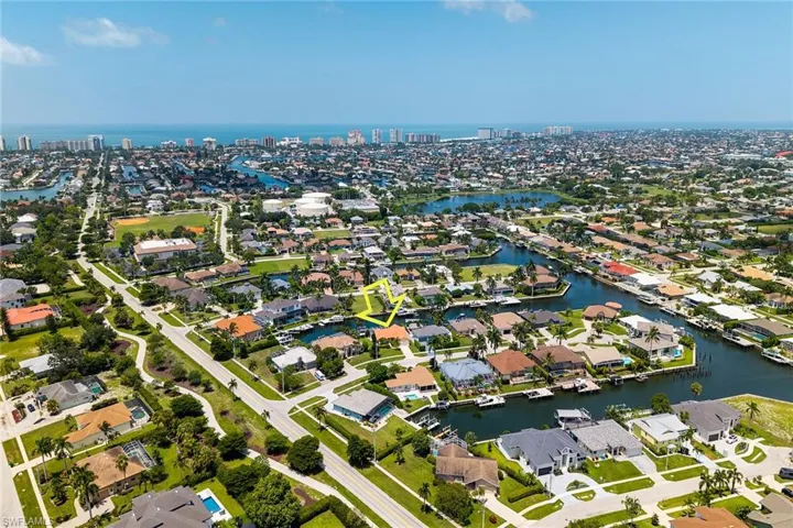 Aerial perspective showcasing a canal-front property within a residential community, featuring a distant coastline and urban skyline