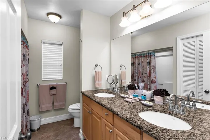 Dual vanity with granite-style countertop, wood-finish cabinetry, and individual sinks with granite vanity top