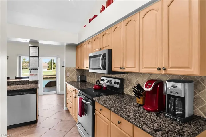 Kitchen featuring light wood cabinetry, stainless steel appliances, granite countertops, and a tiled backsplash