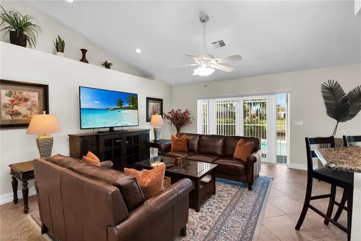 Vaulted ceiling with recessed lighting and a ceiling fan, sliding glass doors, tile flooring, and a breakfast bar with granite countertop