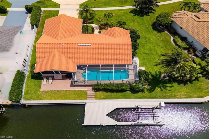 Tile roof residence with a screened pool, waterfront access, private dock, and surrounding green landscaping