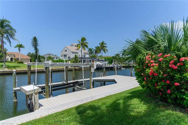 Waterfront property featuring a private boat dock, boat lift, direct canal access, and lush landscaping