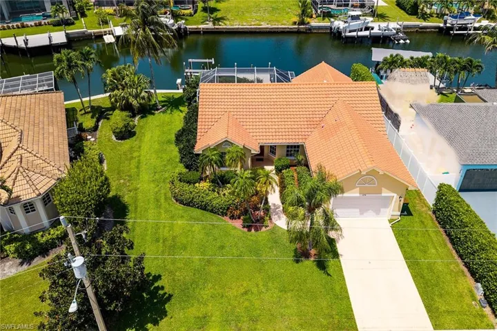 Terracotta tile roof, manicured landscaping, concrete driveway, attached garage, and waterfront access with a boat dock