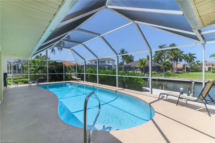 Screened lanai featuring a swimming pool with metal handrails, a spacious pool deck, and canal access with a boat dock