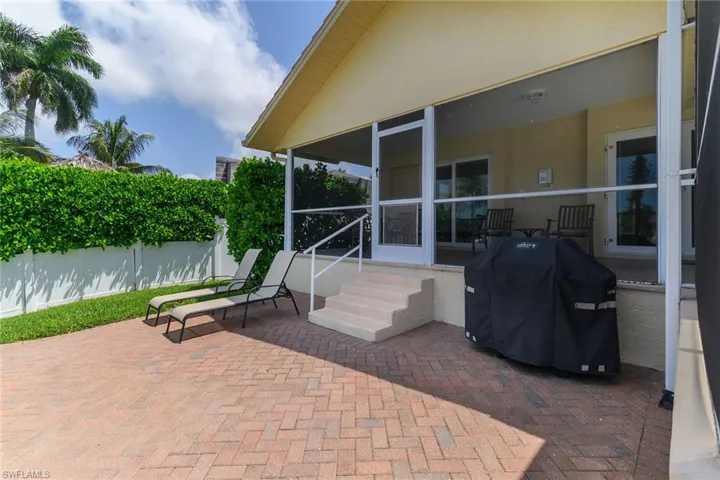 Screened patio with a stepped entry, brick paver patio, privacy fence, and mature landscaping