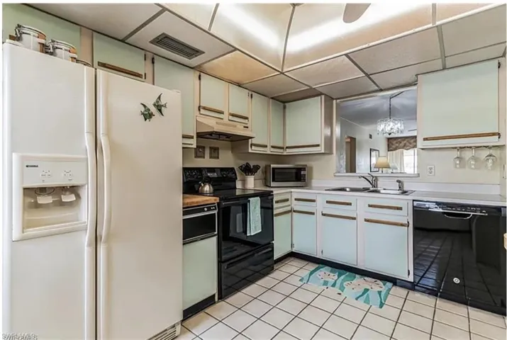 Kitchen with pendant lighting, white cabinets, black appliances, sink, and light tile patterned floors