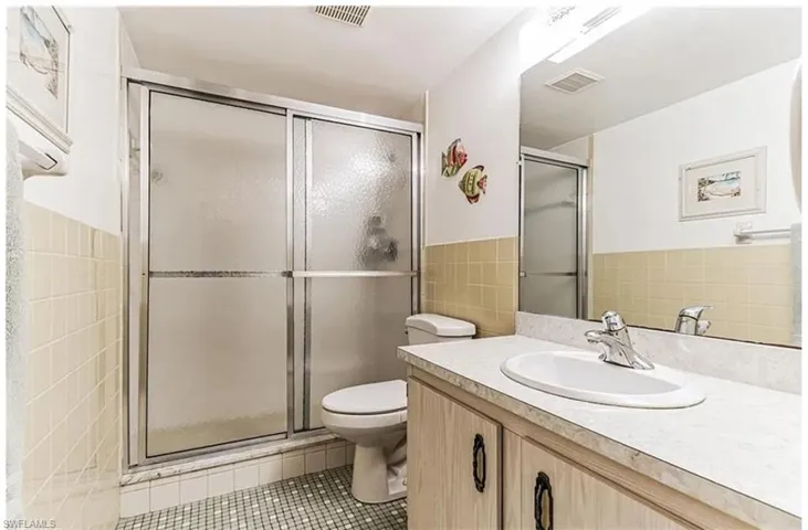 Bathroom featuring toilet, walk in shower, tile walls, tile patterned flooring, and vanity