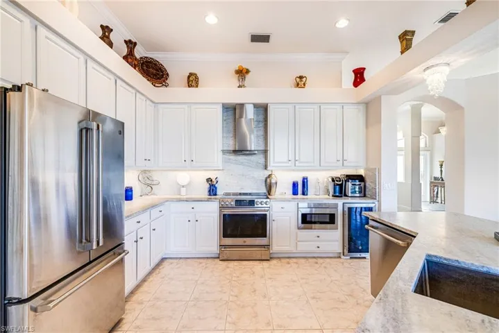 Kitchen featuring arched walkways, stainless steel appliances, white cabinets, crown molding, and beverage cooler