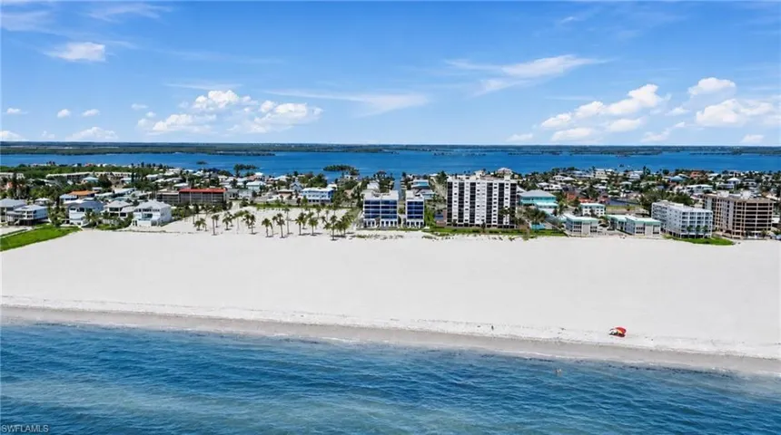 Expansive white sand beach with clear blue water and distant waterfront propertiesExpansive land parcel with direct beach access, surrounded by established buildings and roadways - Virtually Edited Image