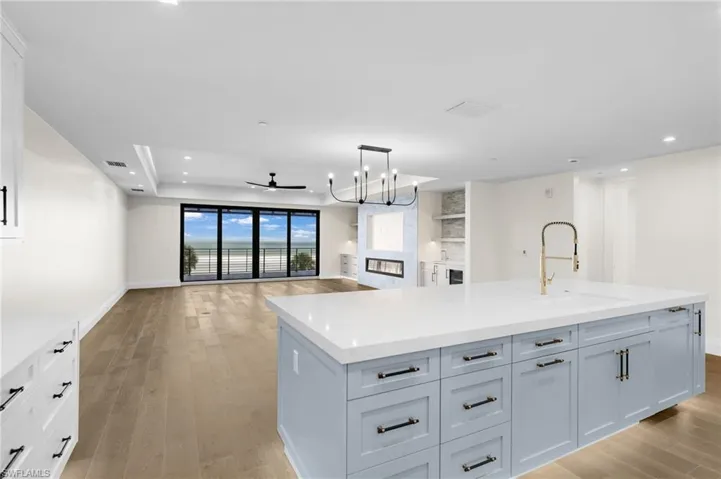 Expansive living space featuring wood-finish flooring, a contemporary fireplace, and a large kitchen island with a gold-tone faucet