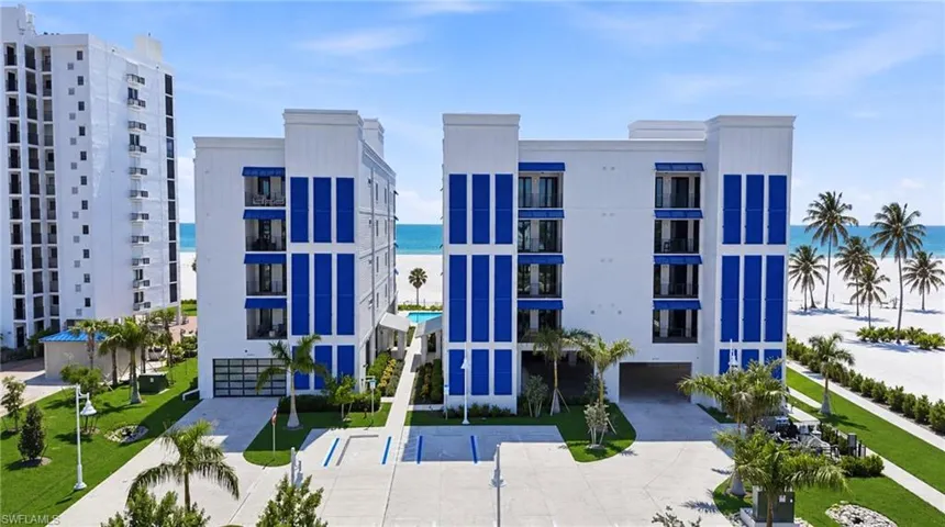 Modern stucco exterior with prominent blue accents, multiple balconies, a covered parking area, and mature palm treesExpansive land parcel with direct beach access, surrounded by established buildings and roadways - Virtually Edited Image