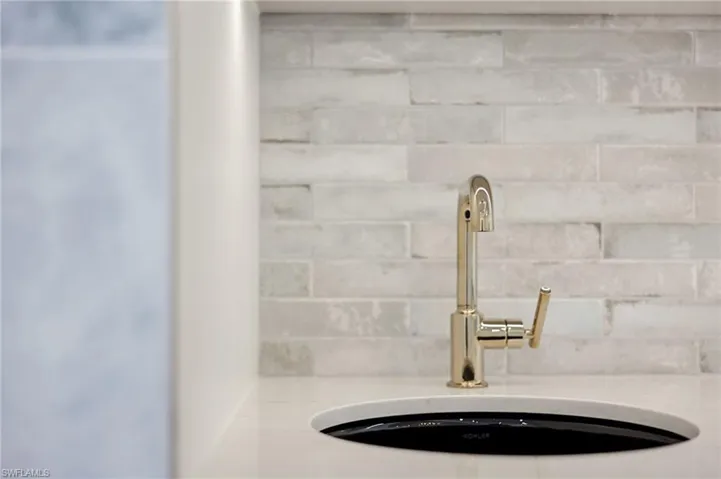 Modern kitchen sink featuring a sleek black vessel basin, polished brass single-handle faucet with an arched spout, and a clean white quartz countertop