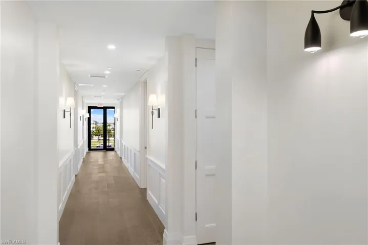 Hallway with wood-finish flooring, recessed lighting, wall sconces, wainscoting, and a paneled door