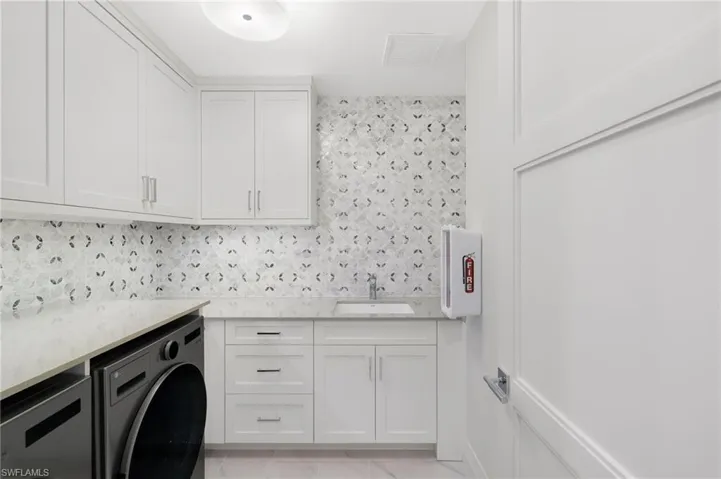 White shaker cabinetry with modern hardware, stone countertops, and a patterned tile backsplash