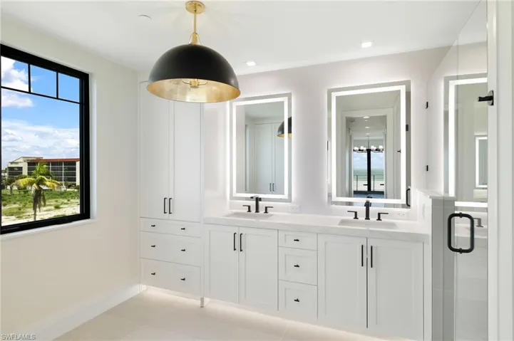 Dual vanity with integrated lighting mirrors, under-cabinet lighting, a built-in linen tower, matte black fixtures, and a glass-enclosed shower
