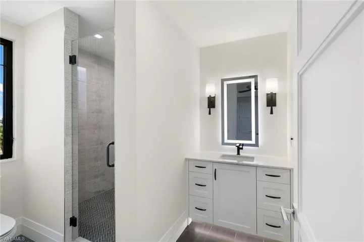 Glass-enclosed shower with chevron tile flooring, a single vanity with stone countertop, and an illuminated mirror
