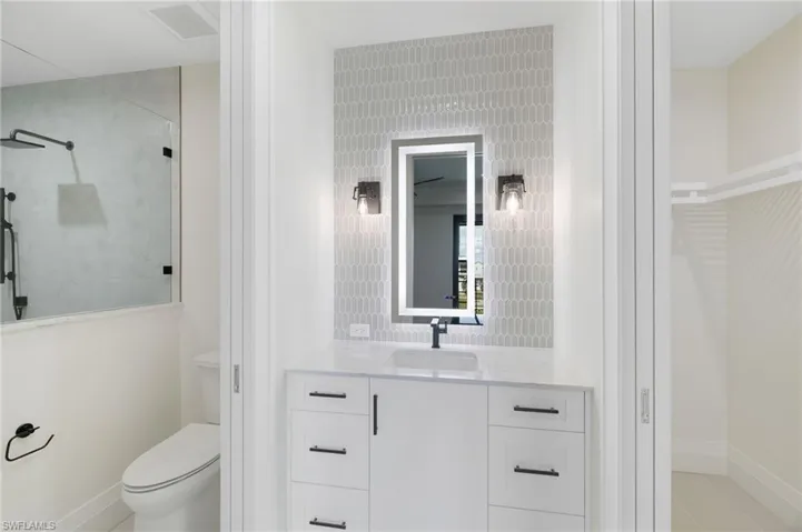 Vanity with a stone countertop, an illuminated mirror, and a tiled accent wall
