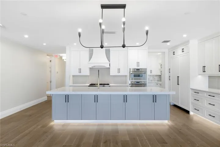 Gourmet kitchen featuring a large central island with under-cabinet lighting, high-end stainless steel appliances, white cabinetry with dark hardware, and wood-finish flooring