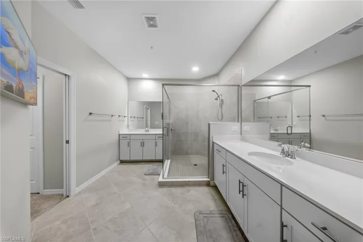Full bathroom featuring two vanities, a shower stall, and recessed lighting
