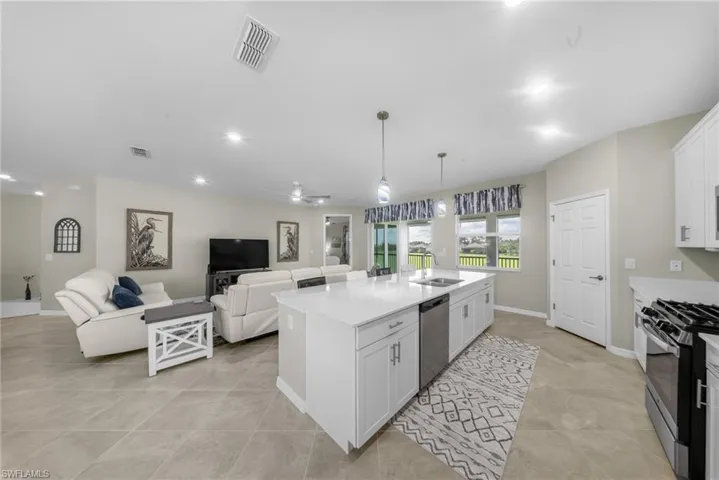Kitchen with white cabinets, open floor plan, light stone counters, stainless steel appliances, and an island with sink