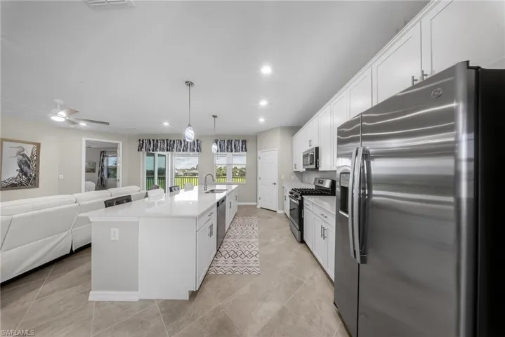 Kitchen featuring stainless steel appliances, a kitchen island with sink, white cabinetry, light stone counters, and a breakfast bar