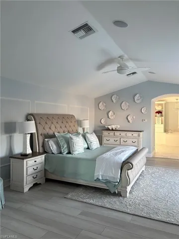 Bedroom featuring arched walkways, light wood-style floors, a ceiling fan, and lofted ceiling