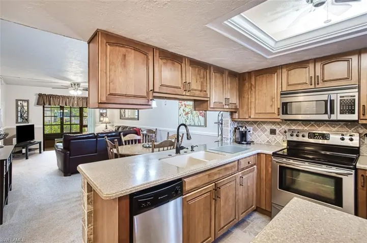 Kitchen with ceiling fan, tasteful backsplash, light carpet, appliances with stainless steel finishes, and kitchen peninsula