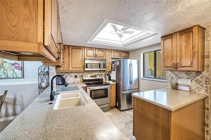 Kitchen featuring backsplash, appliances with stainless steel finishes, sink, and ceiling fan