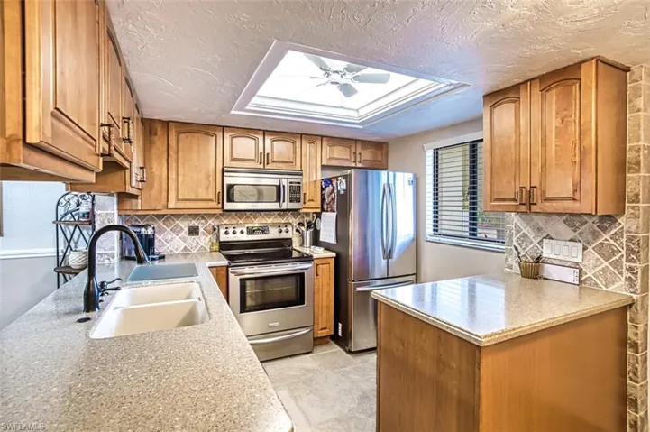 Kitchen with tasteful backsplash, light tile patterned floors, ceiling fan, stainless steel appliances, and sink