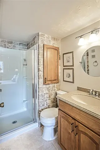Bathroom with vanity, tile walls, a shower with shower door, toilet, and tile patterned flooring