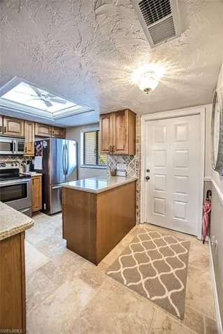 Kitchen featuring decorative backsplash, stainless steel appliances, light tile patterned floors, and a skylight