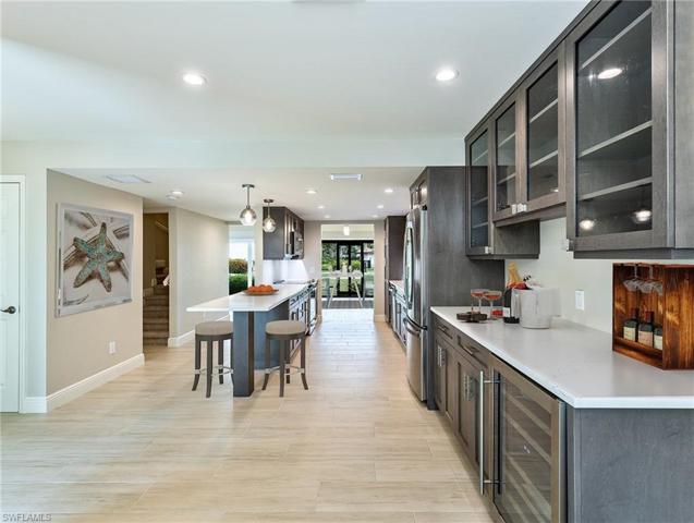 Bar area to kitchen and dining. Hallway to left leads to guest bedrooms, bathroom, powder bath, and stairway to primary bedroom/bathroom suite